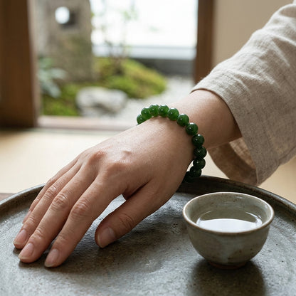 Main portant un bracelet en jade vert, posée sur un plateau en grès près d'une tasse de thé. Décor zen L'Atelier Wen.